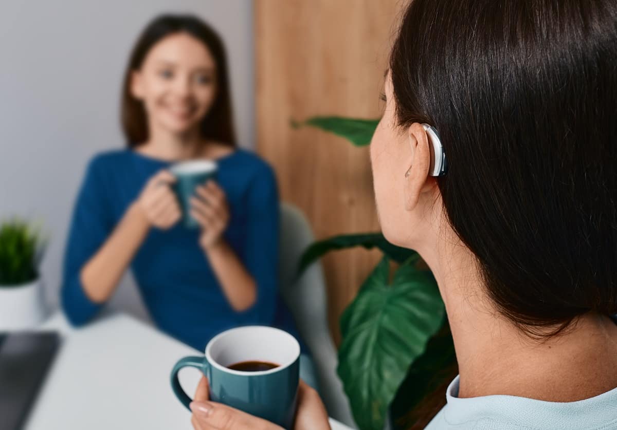 woman with hearing aid having cup of coffee with friend